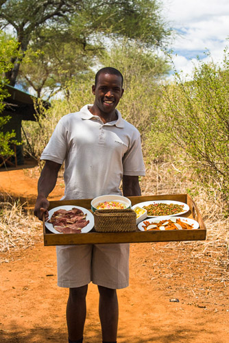 Photo of a smiling african man offering various foods on a tray in a safari camp in Tansania, East Africa