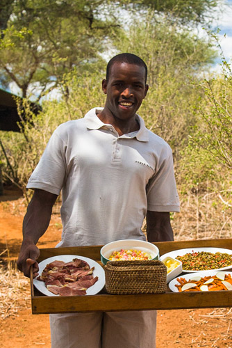 Photo of an african man offering various foods on a tray in a safari camp in Tansania, East Africa