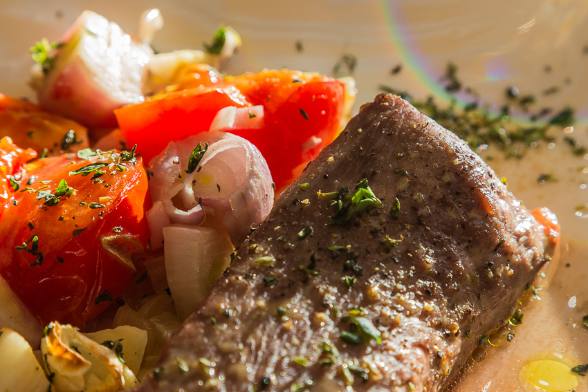 Close up photo of a roasted lamb filet with roasted tomatoes and shallots on a plate